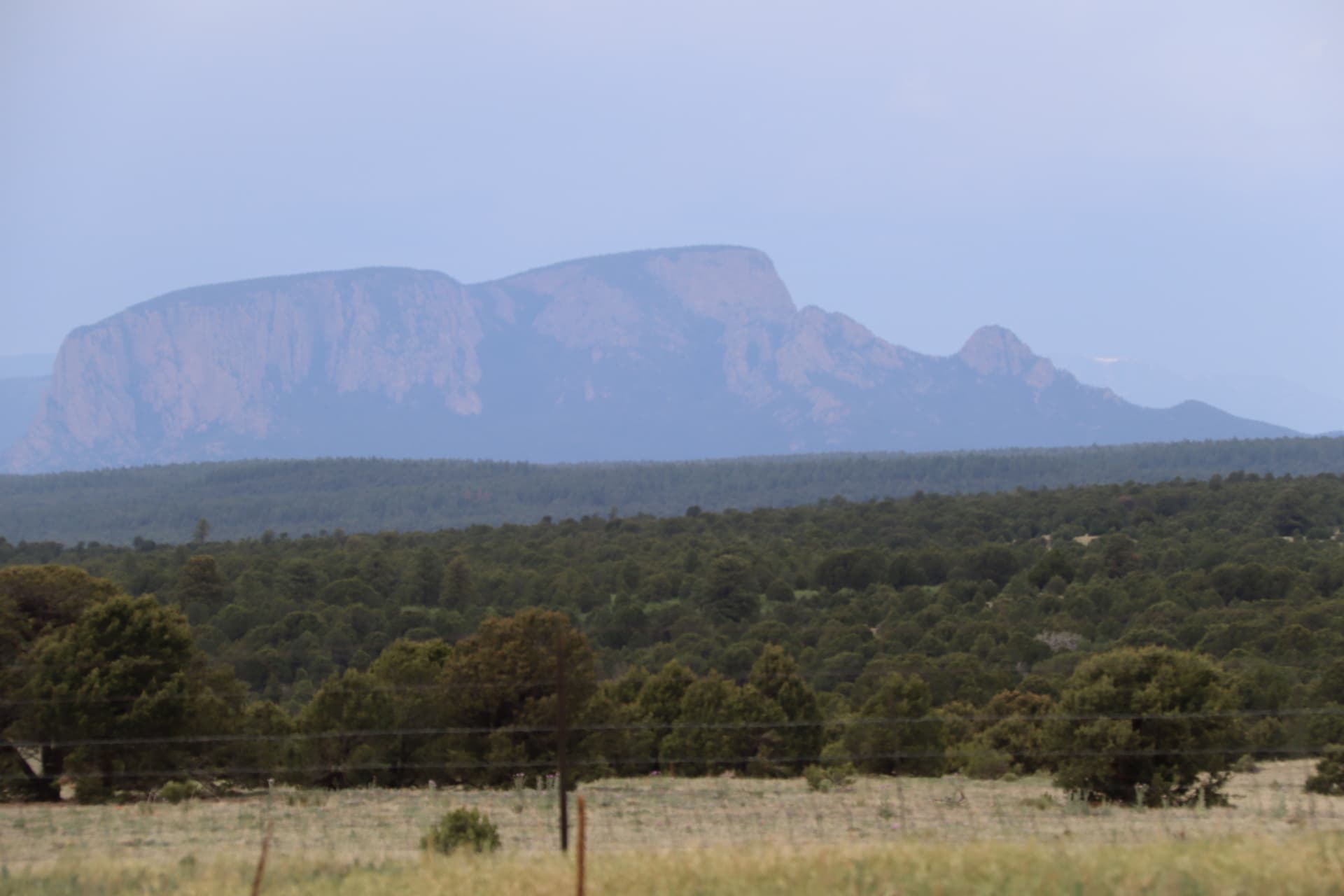 Open high-desert ranchland with pine forests and a flat-topped mesa near Las Vegas, New Mexico